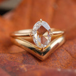 14k yellow gold rose-cut oval diamond solitaire engagement ring, paired with thick 14k yellow gold wedding band in a V-shape. Rings sit on an orange background.