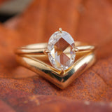 14k yellow gold rose-cut oval diamond solitaire engagement ring, paired with thick 14k yellow gold wedding band in a V-shape. Rings sit on an orange background.