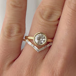 Video of hand modeling a 14k yellow gold round bezel set diamond engagement ring, paired with V-shaped 14k yellow gold and diamond wedding band