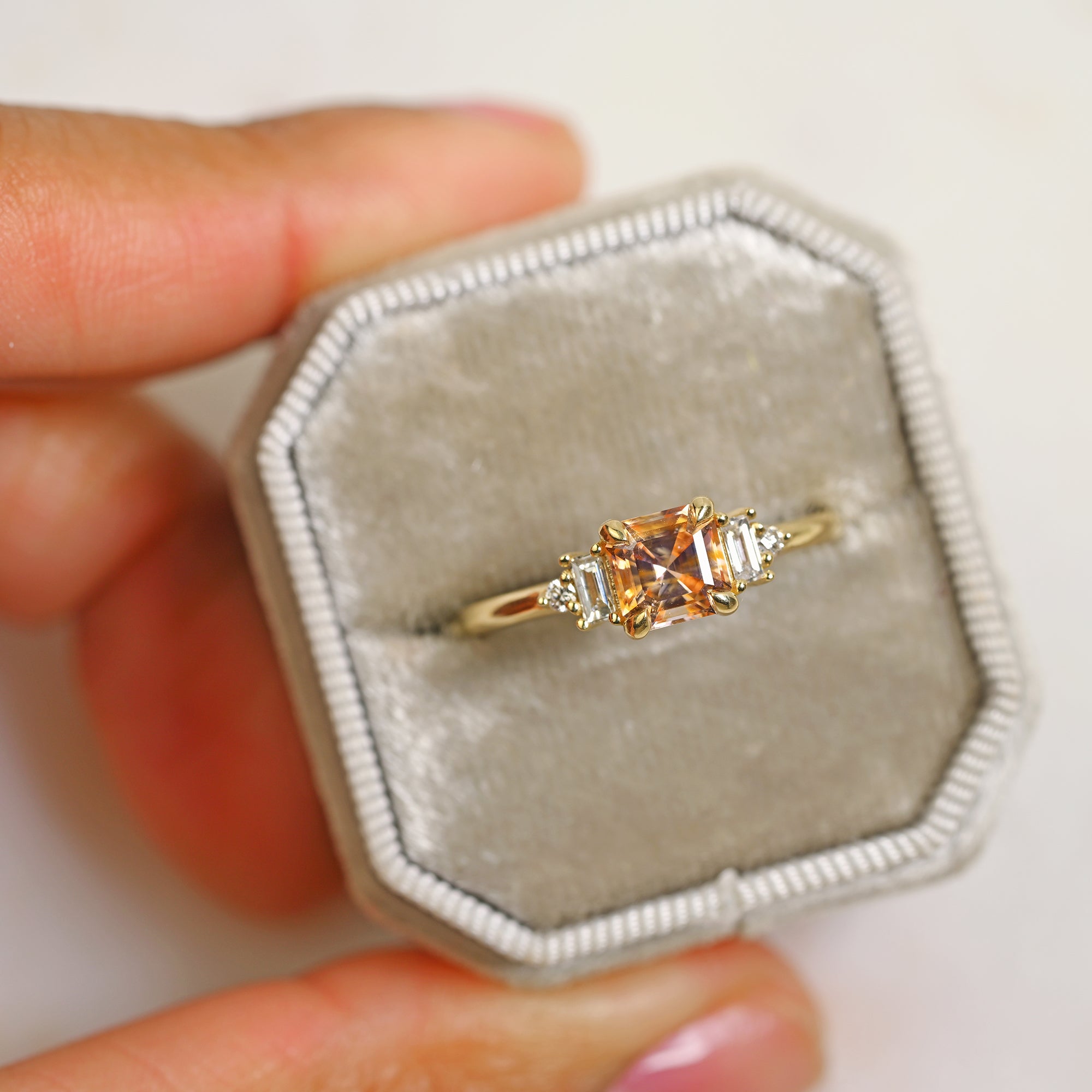 14k yellow gold peach Asscher cut sapphire with round and baguette diamond side stones engagement ring in a gray ring box