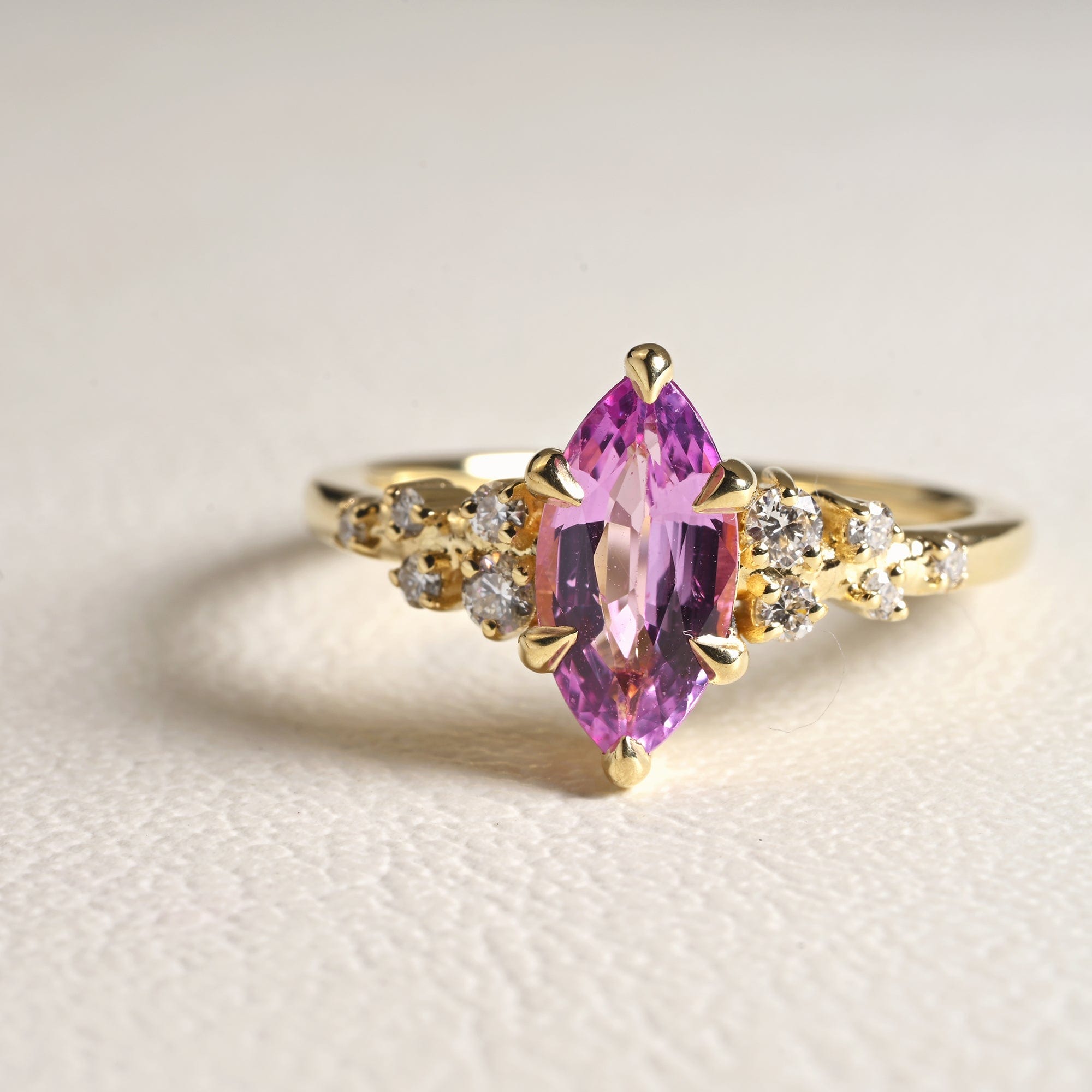 14k yellow gold engagement ring with a bright pink marquise sapphire surrounded by scattered white diamonds