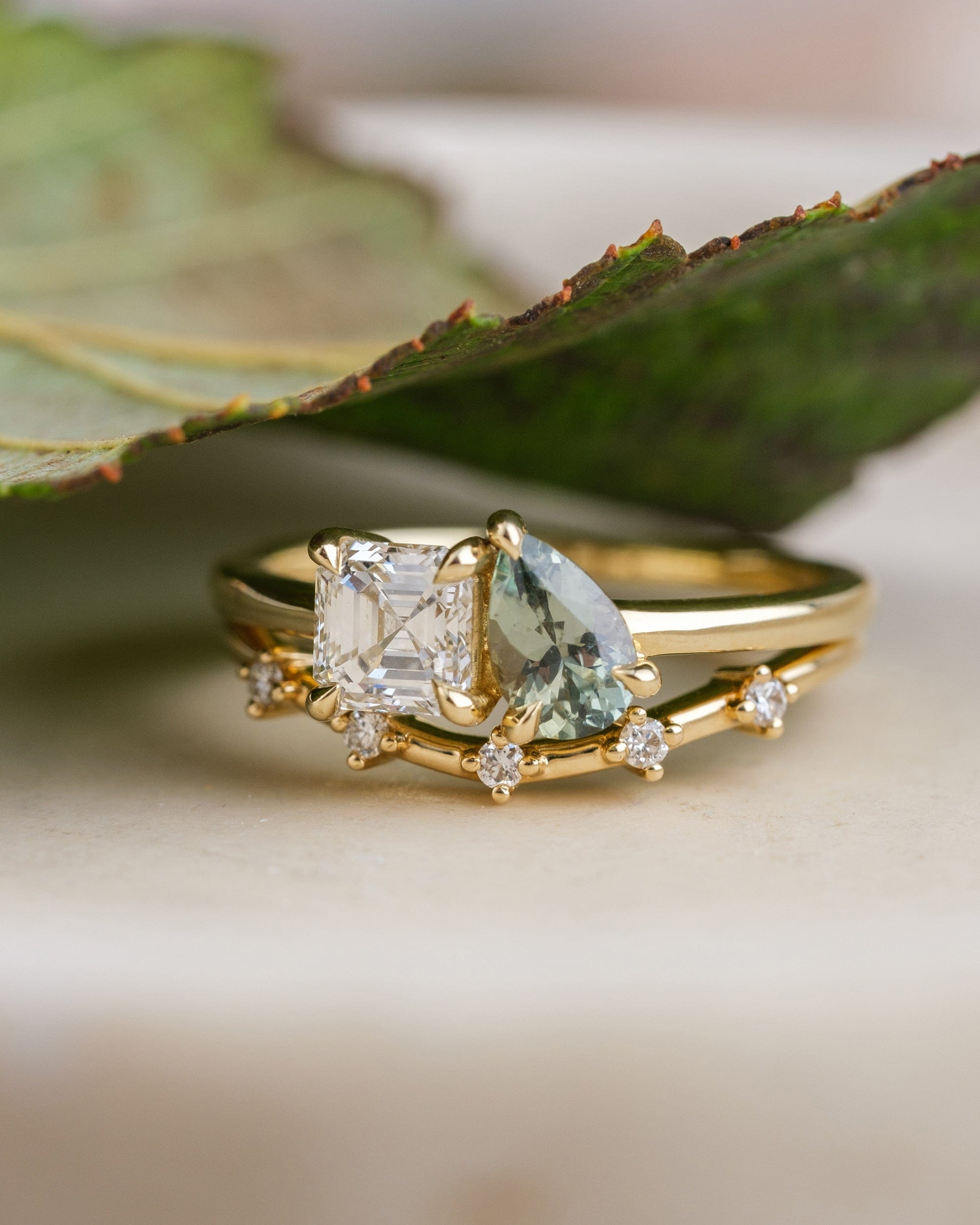 14k yellow gold Toi et Moi ring with an Asscher-cut diamond and sage green pear cut sapphire, paired with a 14k yellow gold band with 5 diamonds