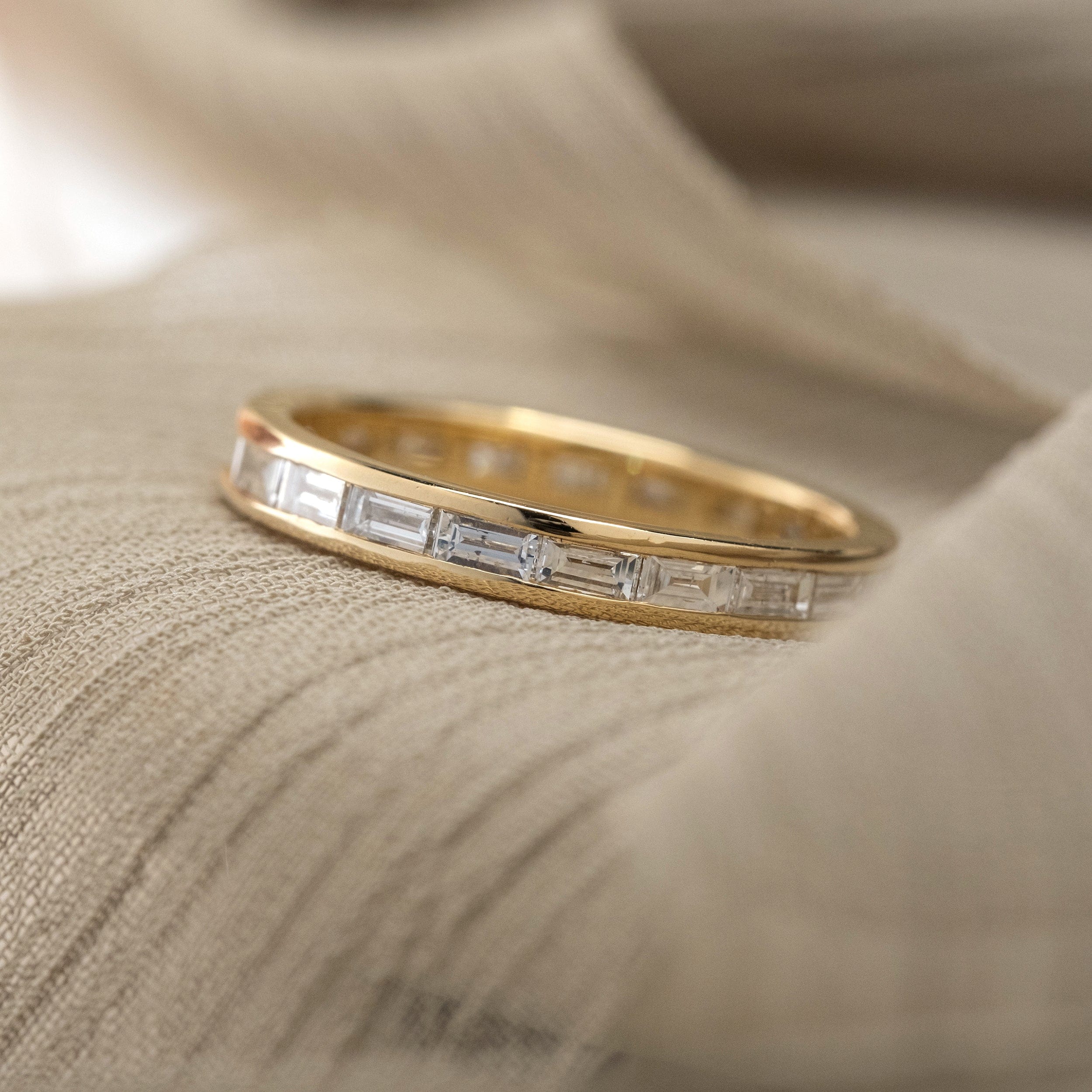 Channel set baguette diamond wedding band in 14k yellow gold sitting on a beige background