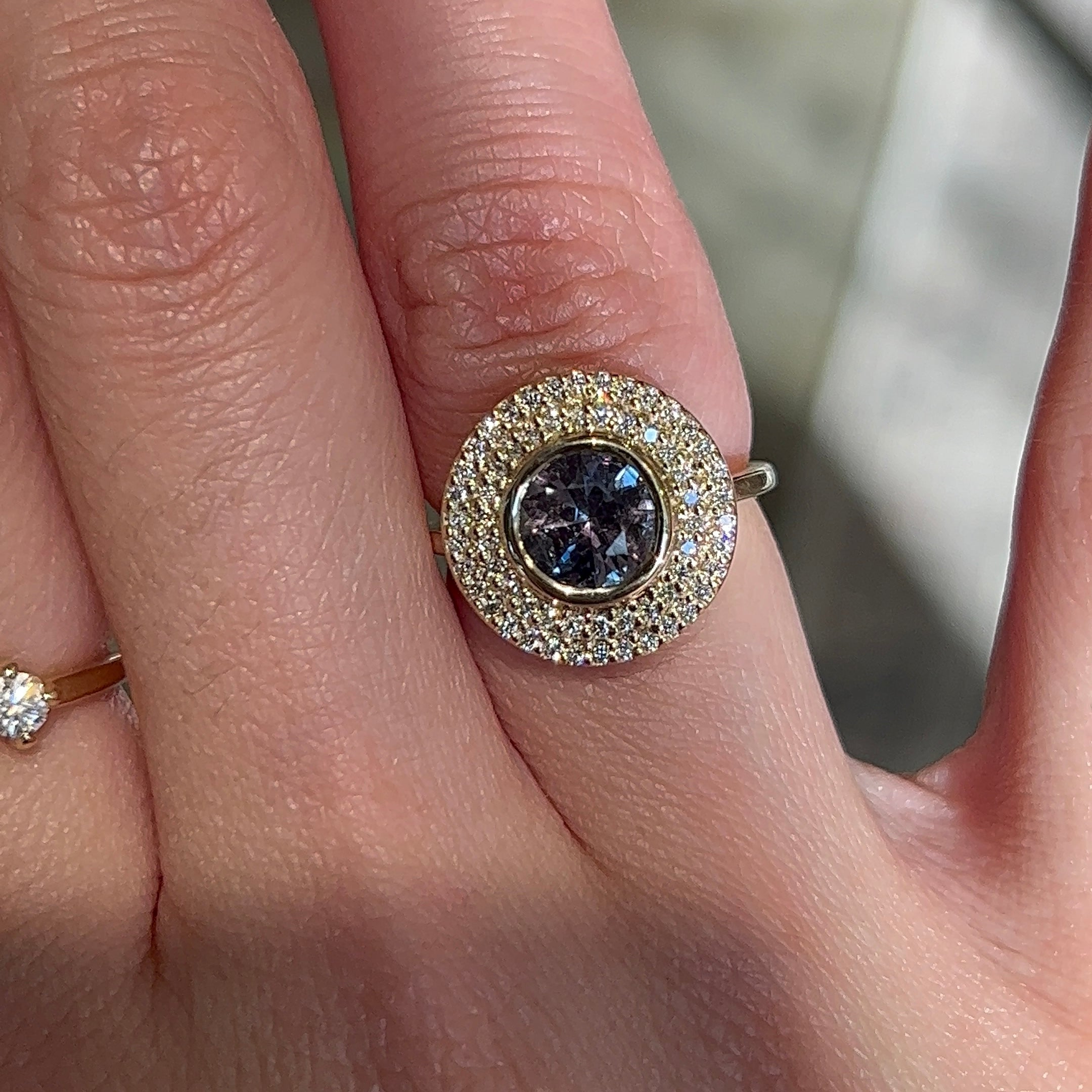 14k yellow gold engagement ring with a round purple sapphire and double halo of diamonds worn on a hand