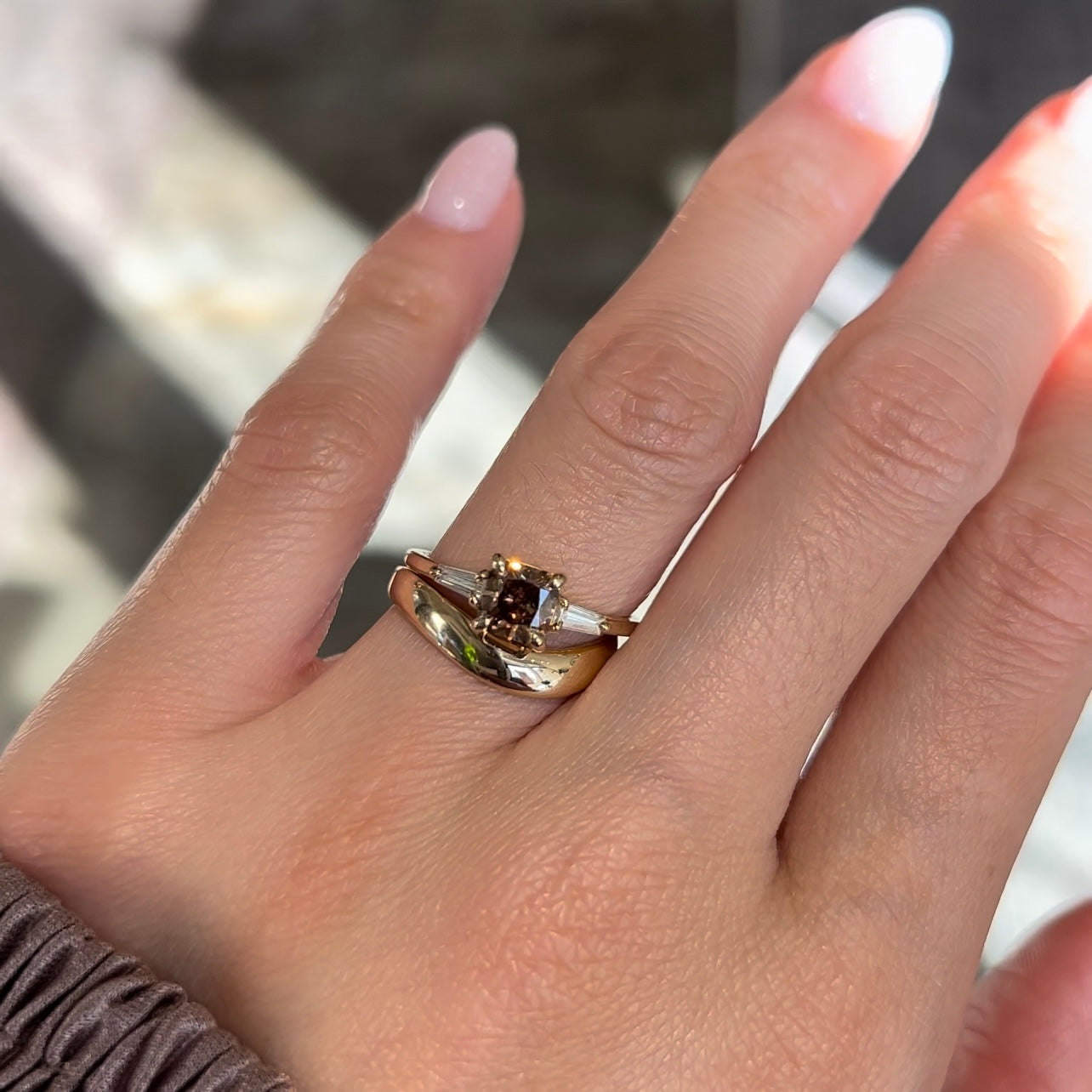 14k yellow gold engagement ring with a fancy brown cushion diamond and tapered baguette diamond accents worn with a thick gold curved wedding band