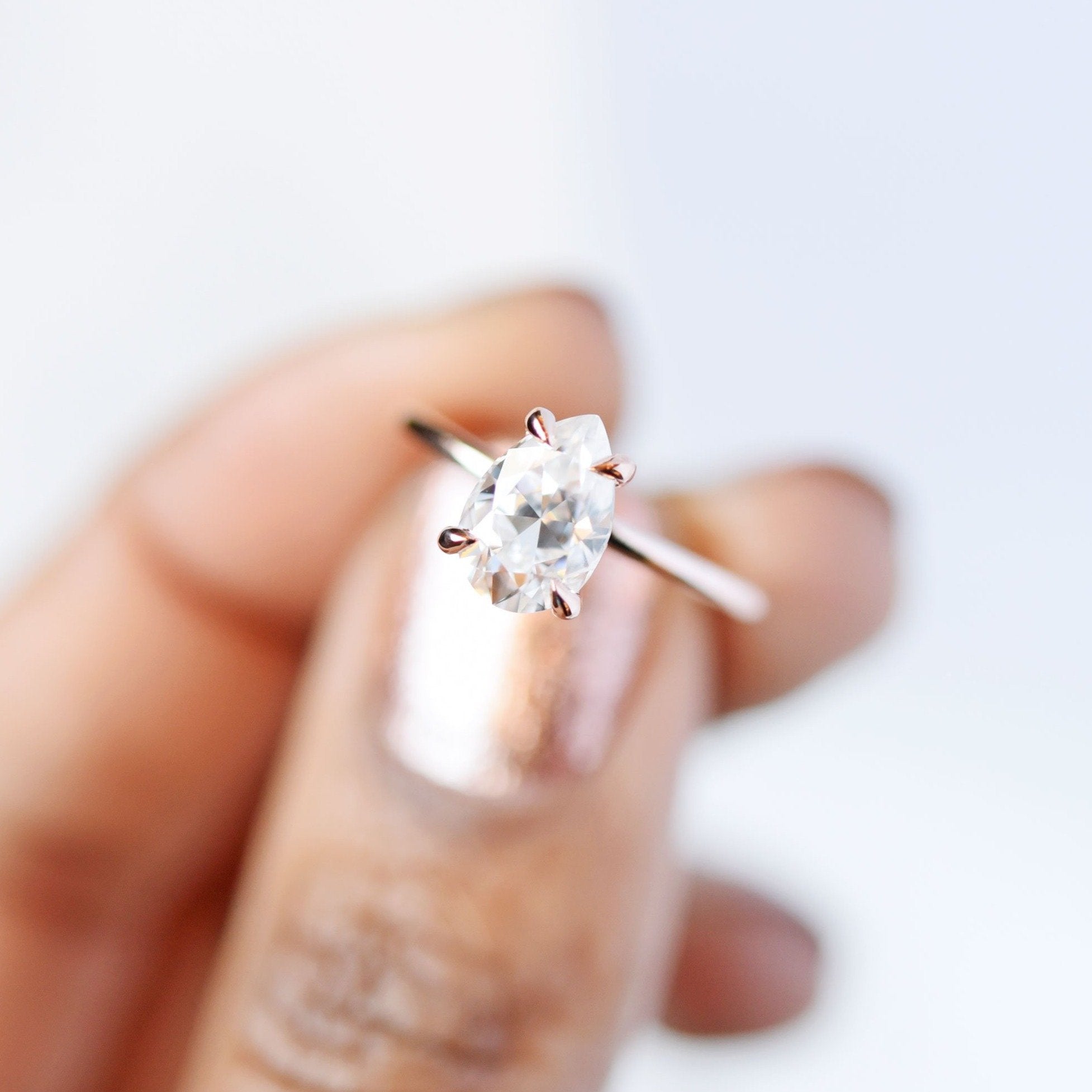 Vera Pear 1.5ct Moissanite Solitaire Engagement Ring held between fingers in an overhead view